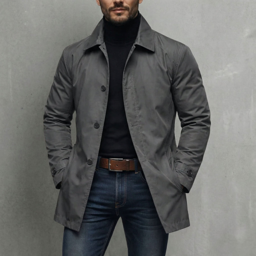Grå frakke til herre med skjortekrave og knapper, båret med sort rullekravetrøje og jeans