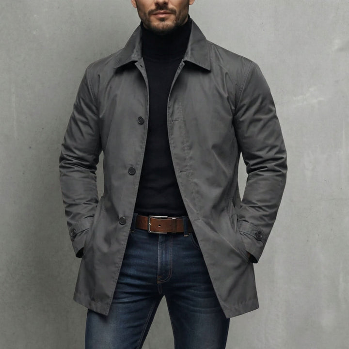 Grå frakke til herre med skjortekrave og knapper, båret med sort rullekravetrøje og jeans