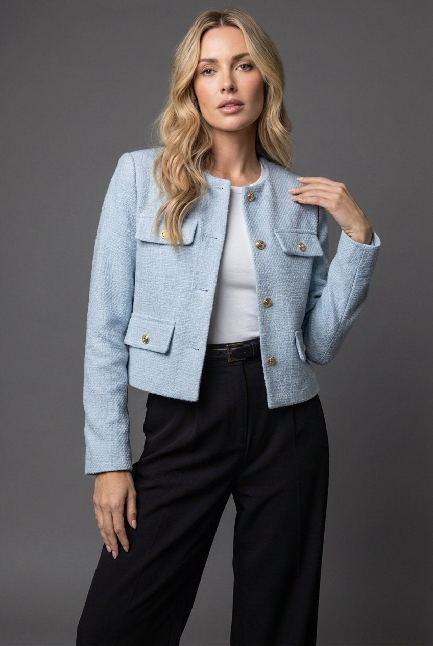 Kvinde i lyseblå kort tweed blazer med guldknapper og sorte bukser