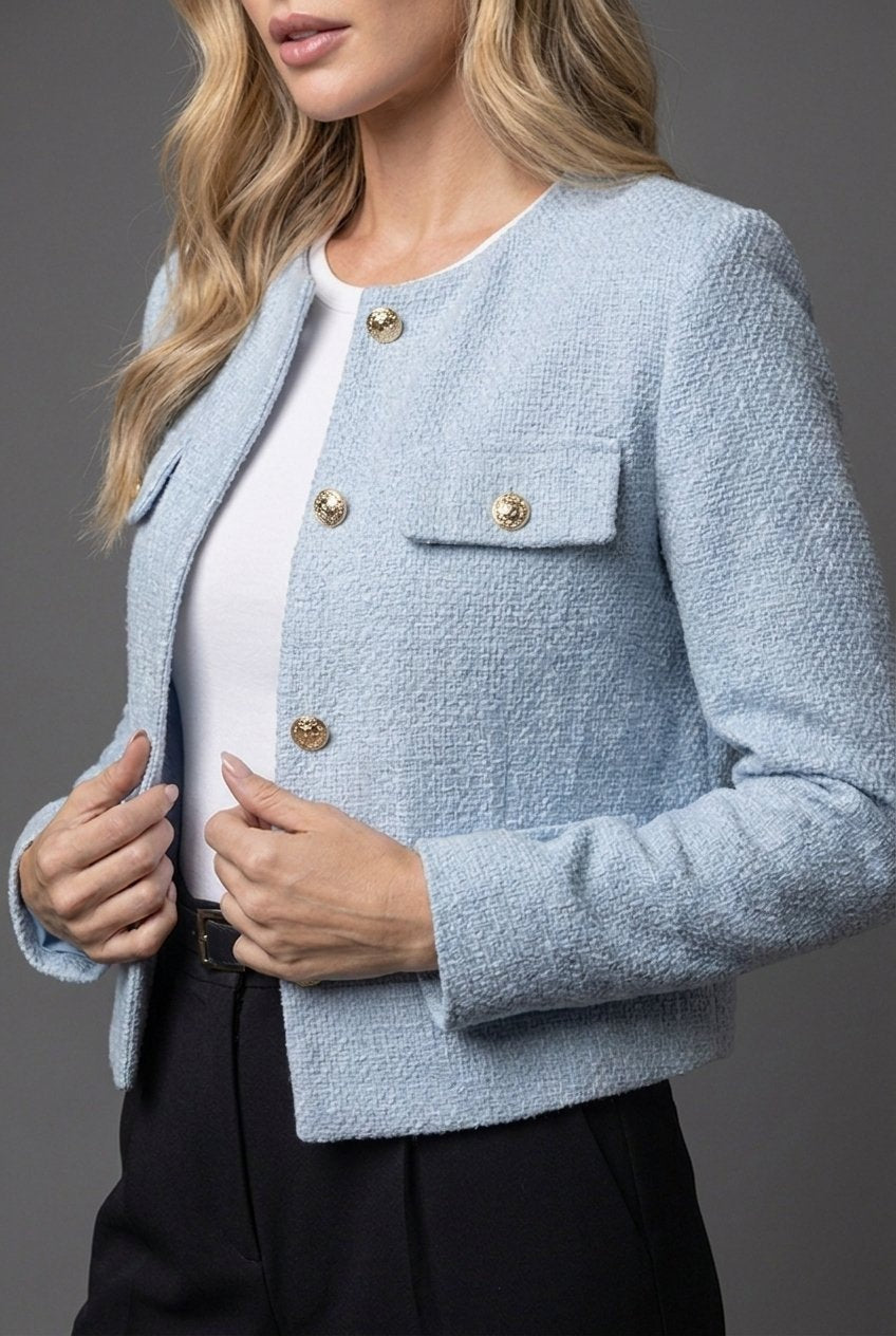 Nærbillede af lyseblå tweed blazer med guldknapper og strukturteksturen