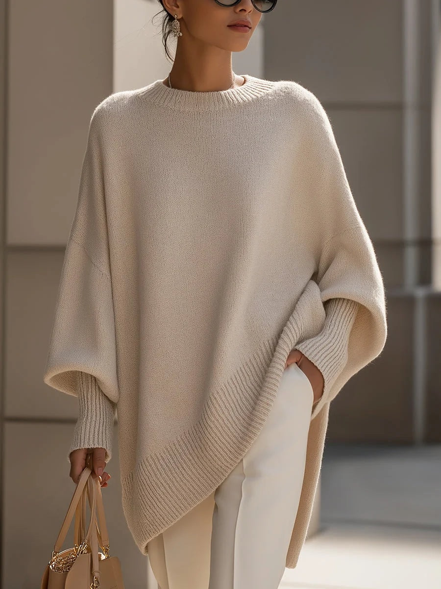 Kvinde i beige oversized strikbluse med flagermusærmer og asymmetrisk kant