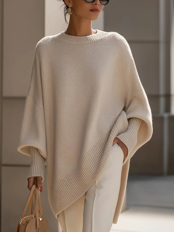 Kvinde i beige oversized strikbluse med flagermusærmer og asymmetrisk kant